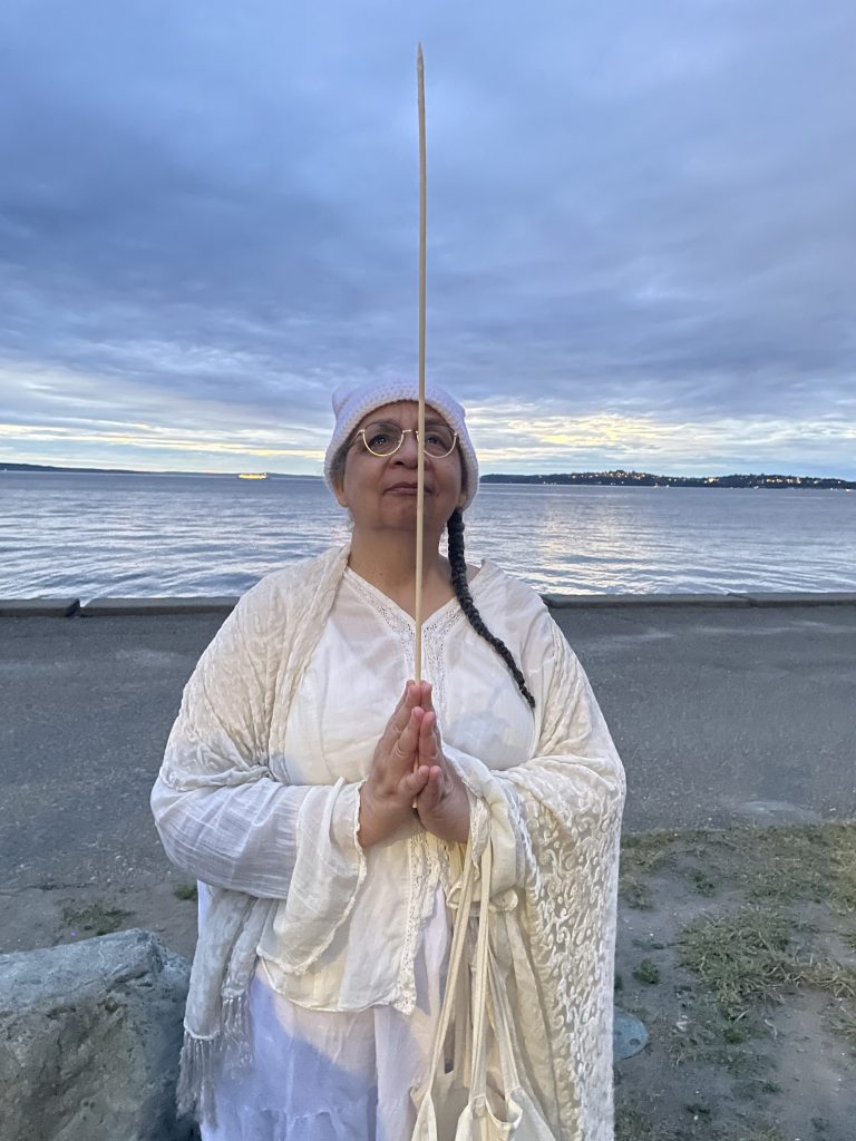 Author photo showing Nisi Shawl on a beach holding a skewer between hands with palms together as in prayer