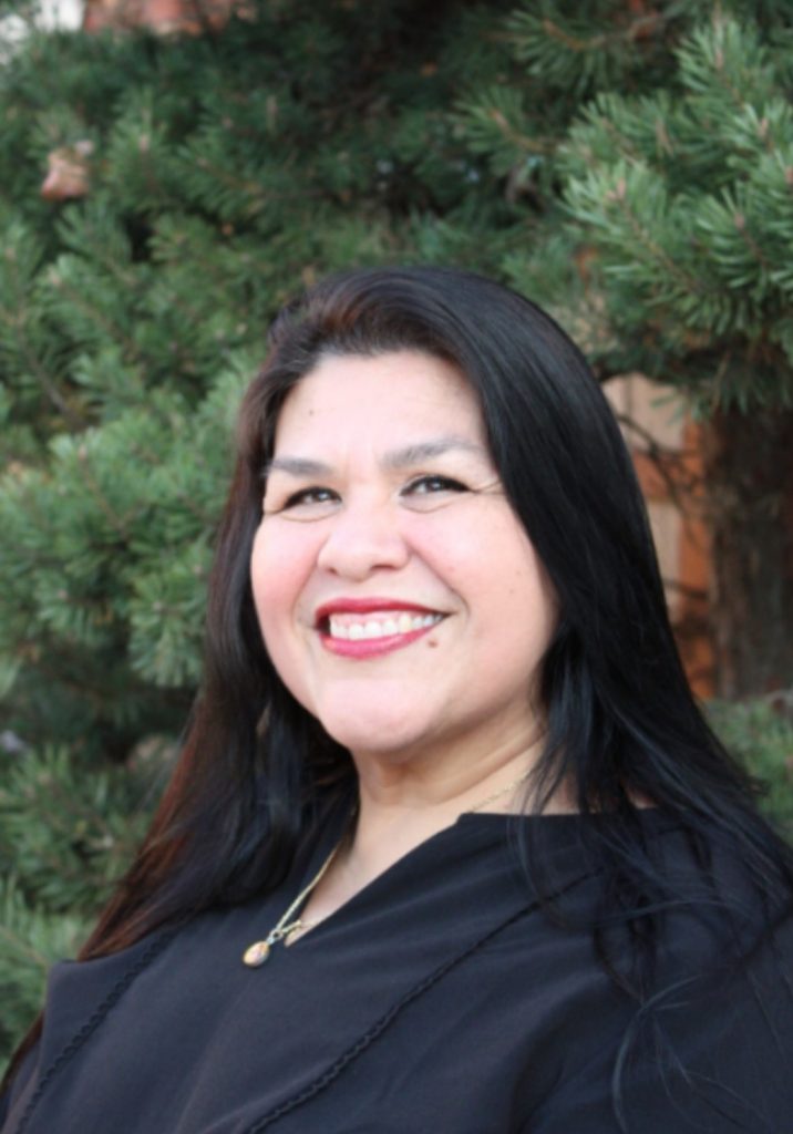 Guadalupe García McCall author photo shoulders up in front of evergreen tree