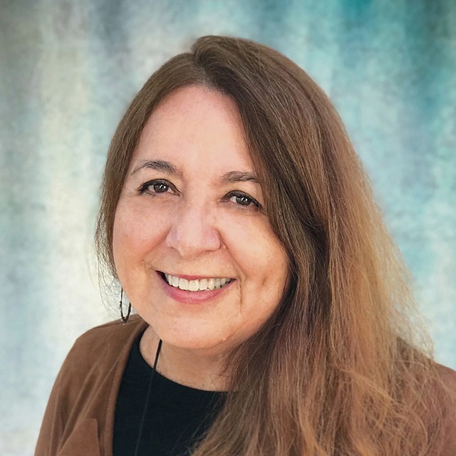 Author photo of Dr. Barbara Flores with long brown hair wearing a black shirt and brown sweater